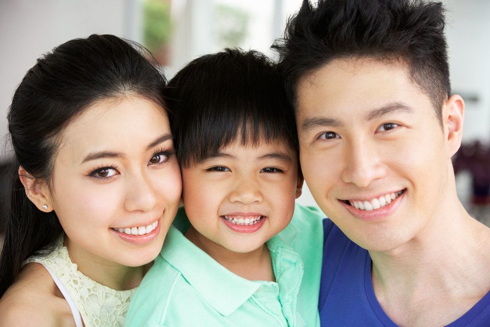 A young family holds one another close while smiling and wearing blue and green shirts.
