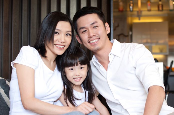A young family wearing white holds one another close while sitting on the couch.